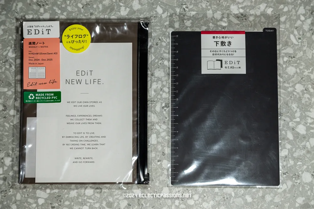 Two packaged planners are shown on a speckled surface. The left planner has a visible label with text about recycled materials, while the right planner is black with Japanese text on the label. Both are part of the EDiT brand collection.