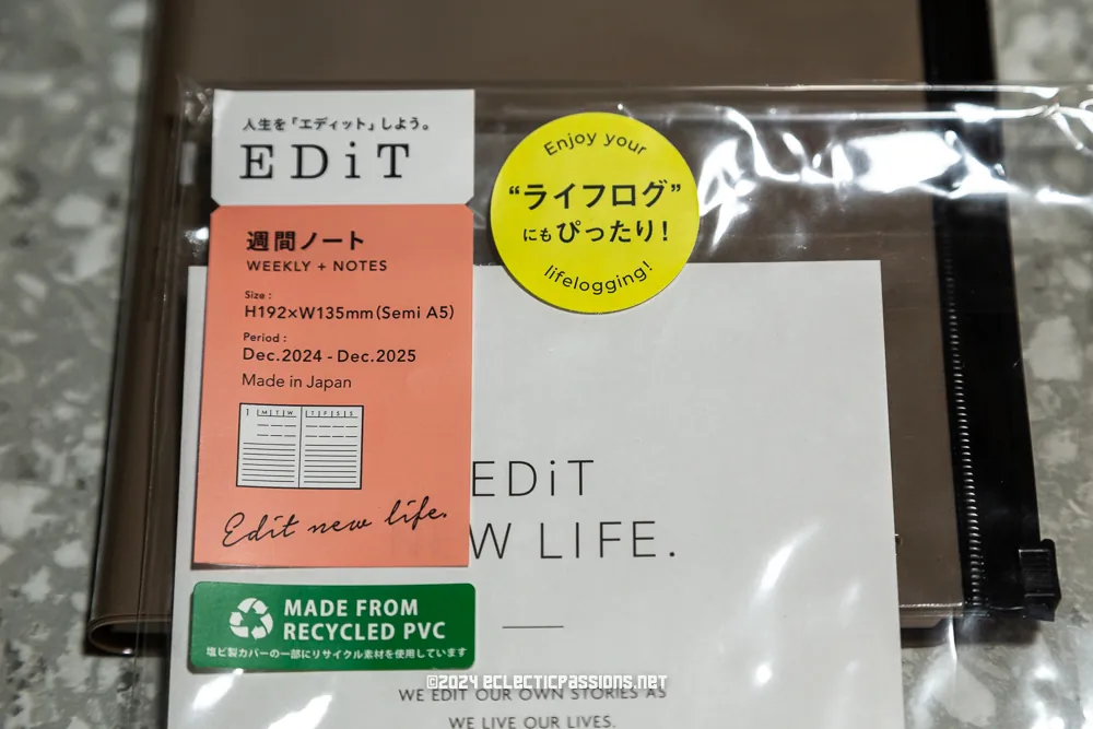 A close-up of a notebook package with various labels. It includes details like "Edit New Life," "Made in Japan," size specifications, and "Made from Recycled PVC." The phrase "Enjoy your lifelogging" is displayed on a circular yellow sticker.