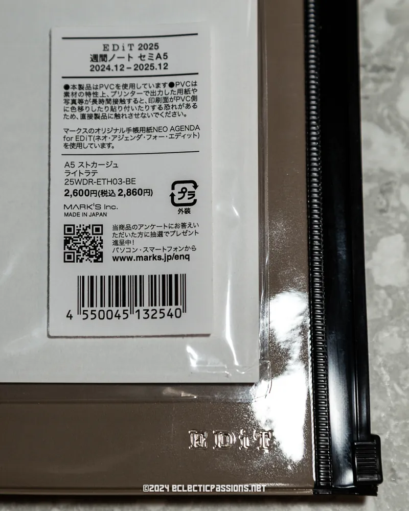 Close-up of a product label on a clear binder. The label includes text in both Japanese and English, indicating item details like "EDIT 2025" and a timeline from 2024.12 to 2025.12. A barcode and pricing information are visible.