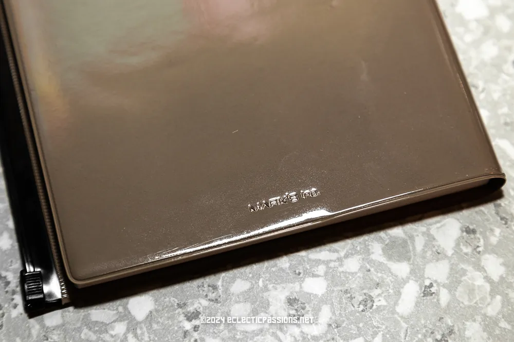 A close-up of a shiny brown file folder on a speckled countertop. The folder is corner-opened, showing its glossy texture. Shadows cast on the surface suggest overhead lighting. Text on the folder reads, 