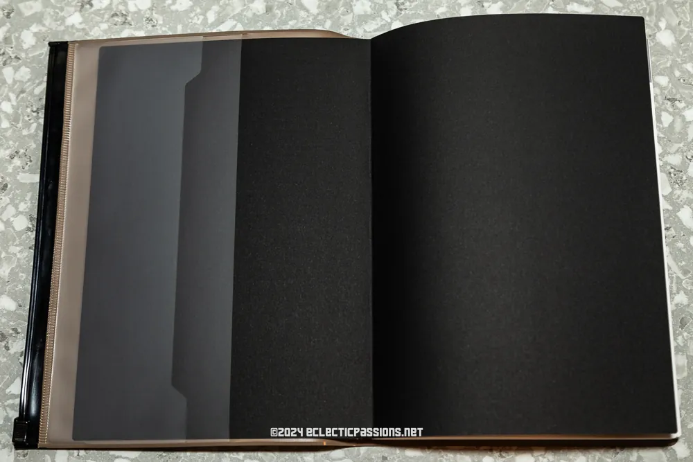 A black binder with open pages displaying dark inserts. The cover is black, and the background is a patterned surface.