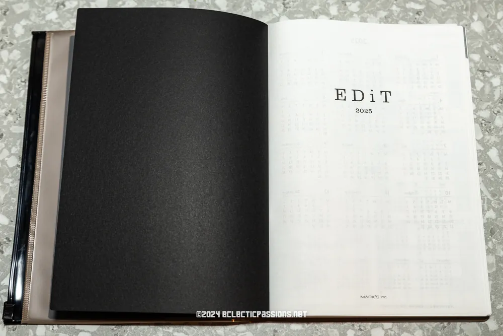 Open book on a speckled surface. Left page is black, and right page is white with the text "EDiT 2025" printed in the center.