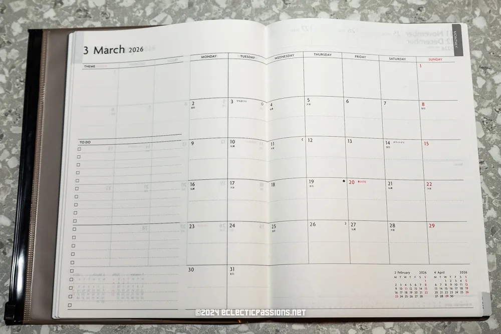 An open planner showing the month of March 2016. The calendar includes days of the week, space for notes on the left, and highlighted Sundays in red. The planner rests on a speckled surface, and a website watermark is visible at the bottom.