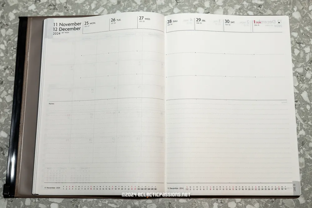 An open planner displaying a weekly schedule from November 25 to December 1, 2024. The pages are blank, set on a speckled gray surface.