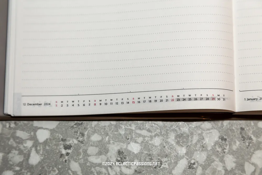 Open planner showing the end of December 2024 and the beginning of January. The calendar displays days and dates with a dotted space for notes. The planner is placed on a textured surface.