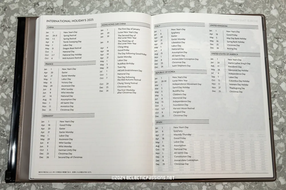 An open book displaying a list of international holidays for 2015, organized by country. The book rests on a gray marbled surface, with text detailing various holidays and their corresponding dates for regions including France, Germany, the UK, and the USA.