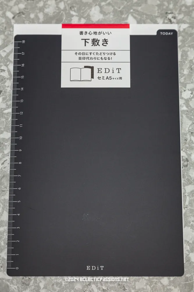 A black EDiT notebook on a textured surface. The notebook has a white label with Japanese text, a small open book icon, and "A5" indicated. A ruler is printed on the left edge, and the word "TODAY" appears at the top right corner.