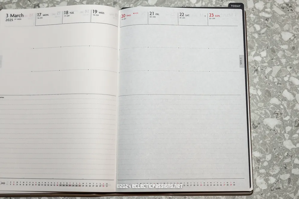 An open planner displaying a weekly layout from March 3 to March 23, 2025, with blank spaces for notes. The pages are set on a speckled gray surface.