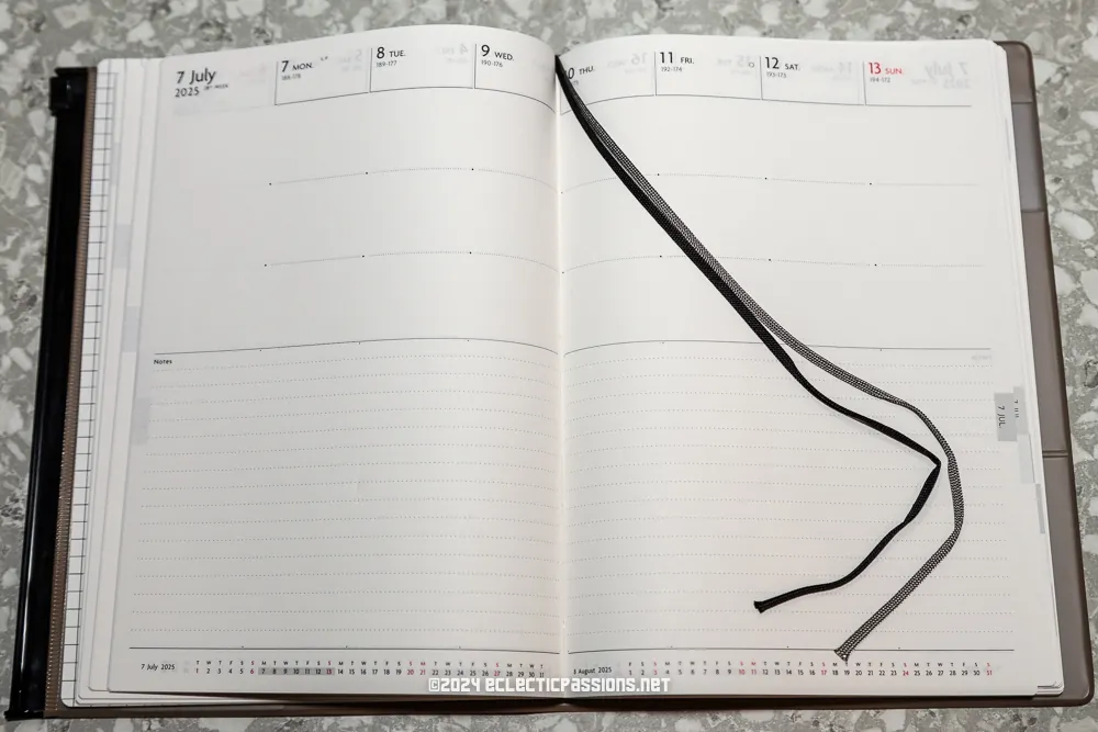 An open planner lies on a textured surface, showing the week of July 7 to July 13, 2025. The pages are blank with a black bookmark ribbon placed across them.