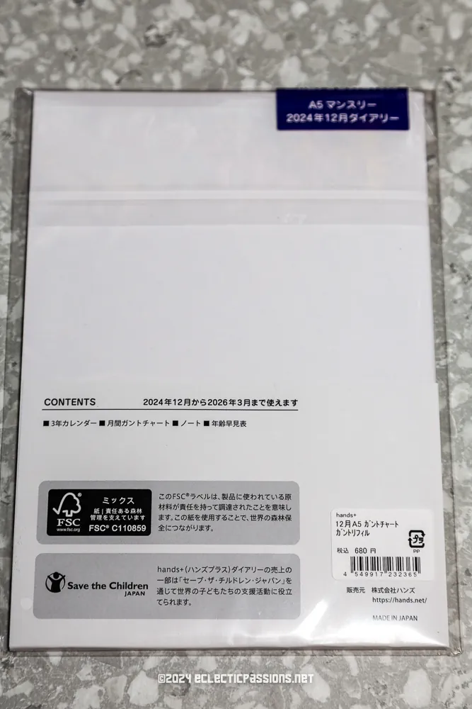 Back cover of a Japanese monthly planner, showing details like the price and contents in Japanese text. It includes logos for FSC certification and Save the Children Japan. Background is a gray, textured surface.