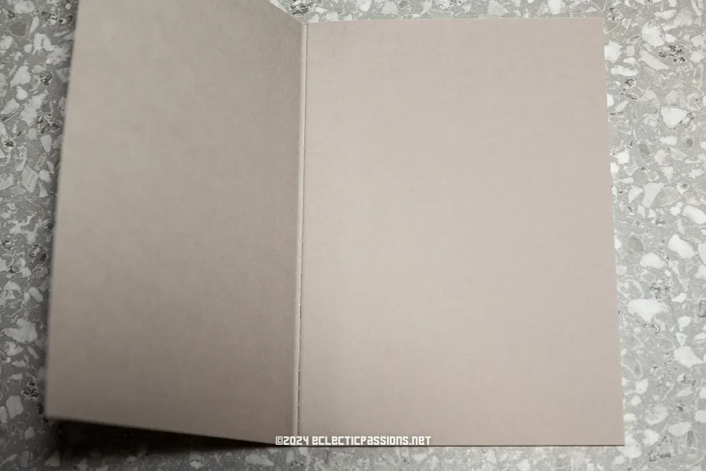 An open blank card lies on a terrazzo countertop. The card is plain with a solid color, creating a simple and minimalist appearance.