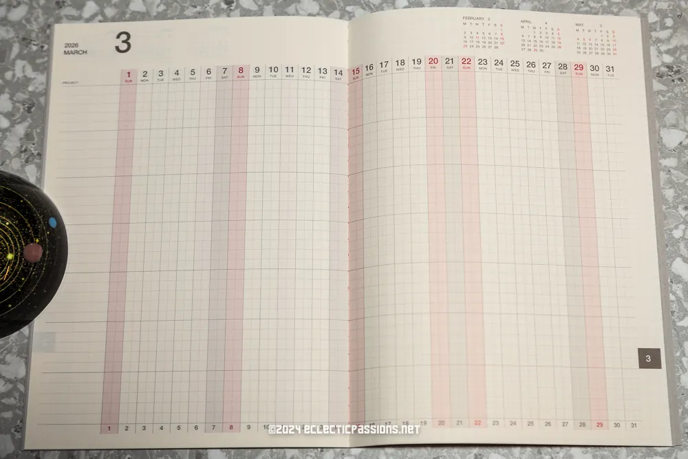 Open planner showing a March 2024 calendar spread with grid lines for each day. The days of the week are listed across the top, and the month and year are noted at the top left. A decorative object is partially visible on the left side.