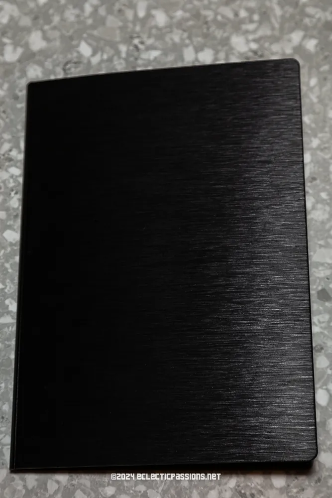 A closed black notebook with a textured cover lies on a speckled gray surface.