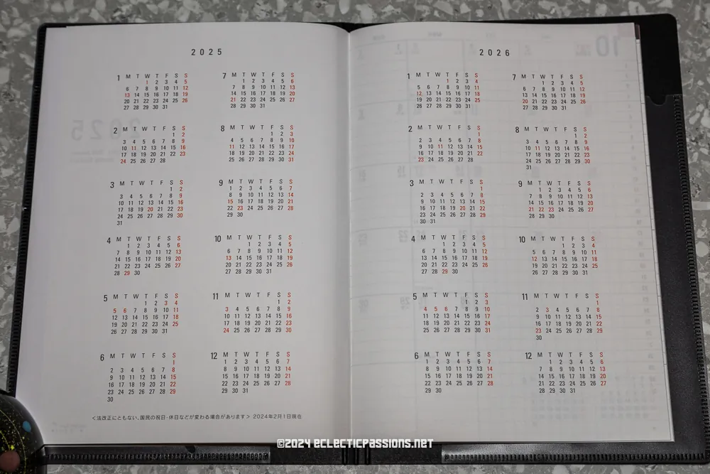 Open planner displaying calendars for the years 2025 and 2026 on a gray textured surface. The planner shows months arranged in a grid layout with days of the week headers.
