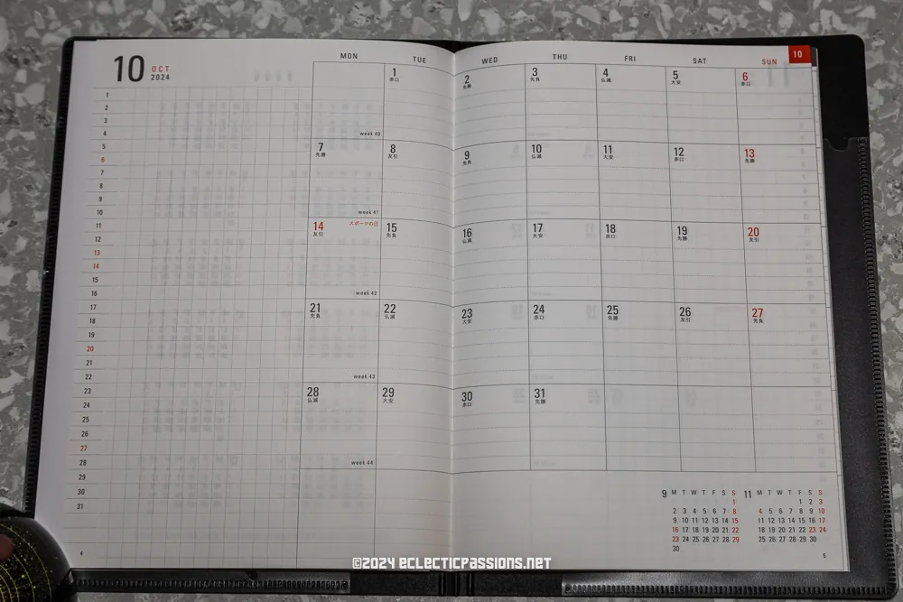 An open planner lays on a gray speckled surface, displaying a monthly calendar for October 2024. The calendar is blank with dates marked in a grid, spanning from Monday to Sunday. A small calendar for the following month is visible at the bottom.