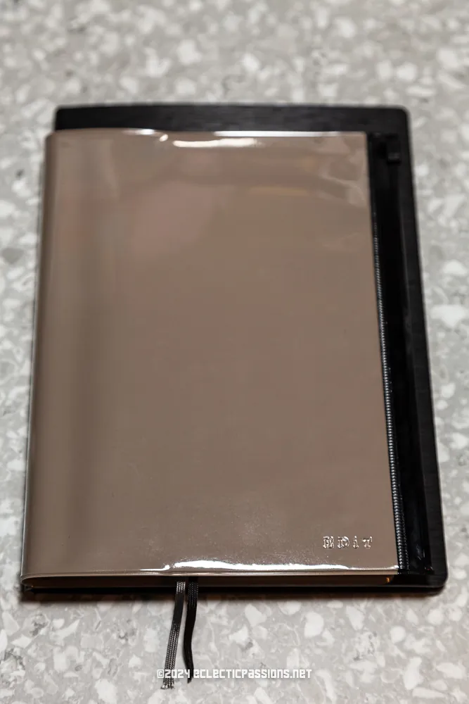 A reflective, metallic journal with a black spine and a protruding ribbon bookmark is placed on a speckled surface. The word "Diary" is embossed in the bottom right corner.